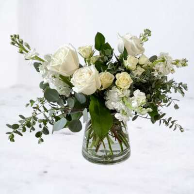 White rose and stock arrangement with foliage in a clear glass vase