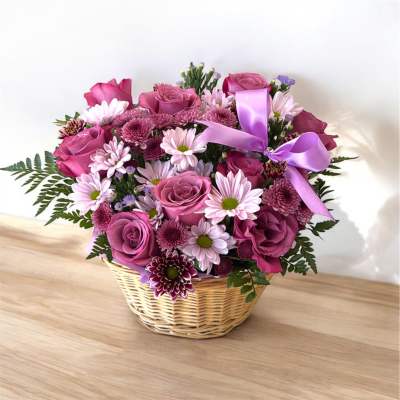Basket arrangement of mauve roses and pink daisies with a purple ribbon bow