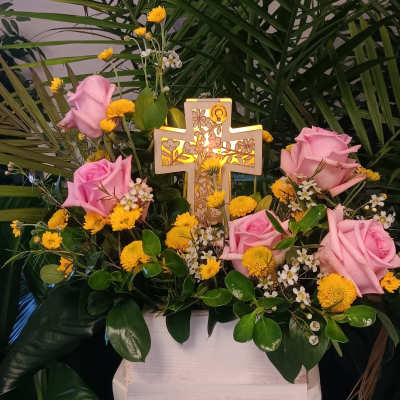 Pink roses and yellow flowers arranged around a lit decorative cross
