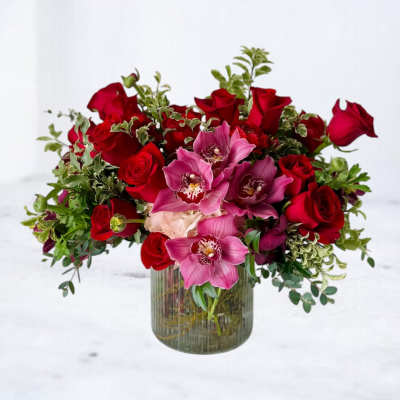 Red roses and pink orchids in a ribbed glass vase