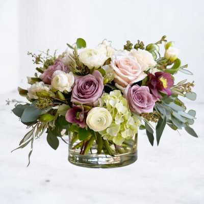 Low arrangement of pastel roses, ranunculus, and green hydrangeas in a clear glass vase
