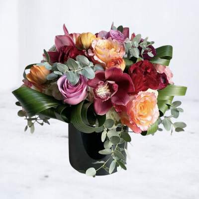 Mixed bouquet of roses, orchids, and peonies in a black vase