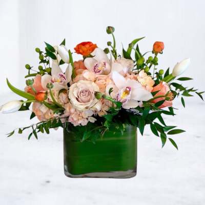 Low peach and white arrangement with roses, orchids, and tulips in a green-lined square glass vase