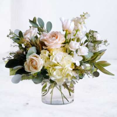 Low glass vase with white hydrangeas, peach roses, and other white flowers in a soft, airy arrangement