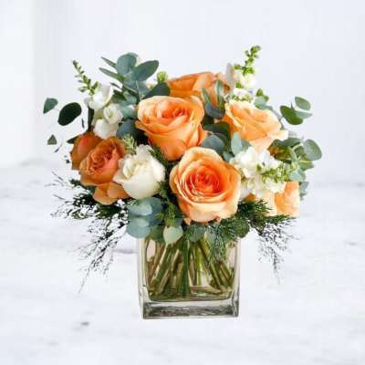 Peach and white roses arranged in a clear square glass vase