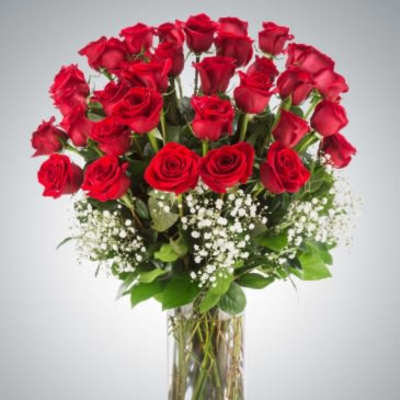 Tall arrangement of red roses with white filler flowers in a clear glass vase