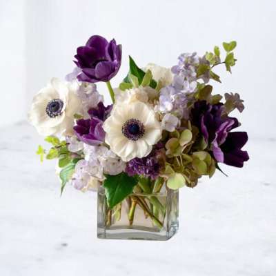 Low arrangement of purple and white anemones with mixed blooms in a clear glass cube vase