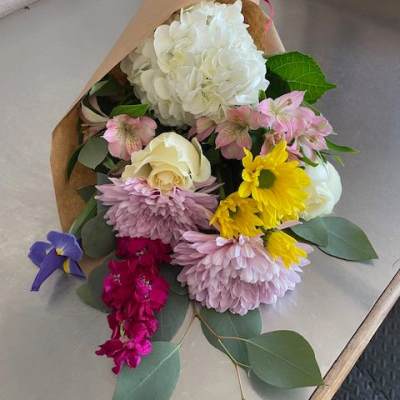 Mixed bouquet of white, pink, yellow, and purple flowers wrapped in brown paper