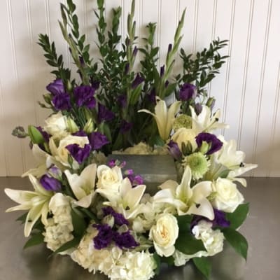 White lilies and purple flowers arranged around a rectangular container