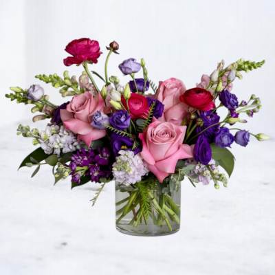 Pink roses with purple lisianthus and red ranunculus in a clear glass vase