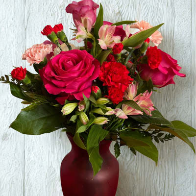 Pink roses and red carnations arranged in a burgundy vase