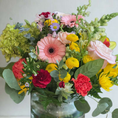 Mixed bouquet of pink, yellow, and purple flowers in a glass vase