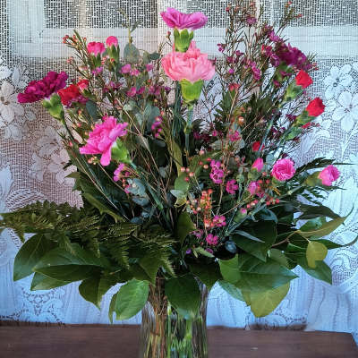 Pink and purple carnations in a clear glass vase with mixed greenery