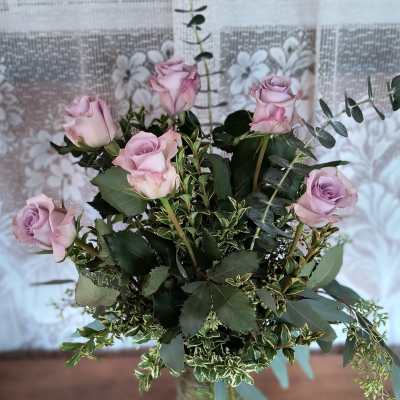Lavender roses arranged in a clear glass vase with mixed greenery