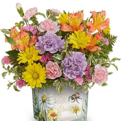 Mixed bouquet in a square glass vase with pink, yellow, orange, and lavender flowers.
