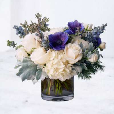 Low arrangement of white roses, hydrangeas, and purple anemones in a clear glass cylinder vase