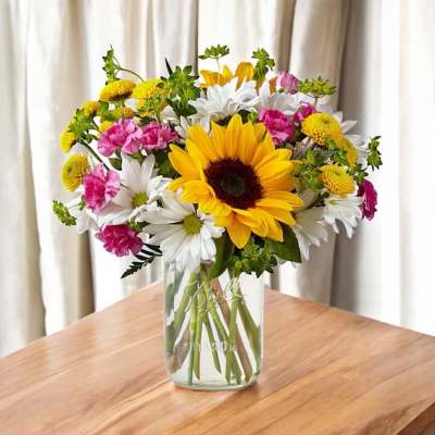 Bouquet of sunflowers, white daisies, pink carnations in a glass vase
