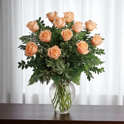 Peach roses arranged in a clear glass vase with mixed greenery