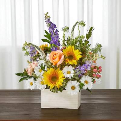 Mixed bouquet in a white rectangular vase with sunflowers, roses, and daisies