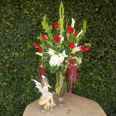 Tall bouquet of red roses and white lilies in a glass vase with a fairy figurine