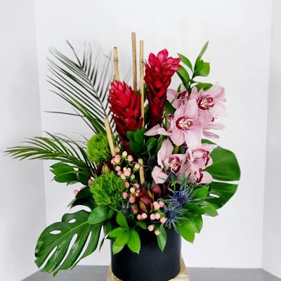 Tropical arrangement with pink orchids and red ginger in a black vase