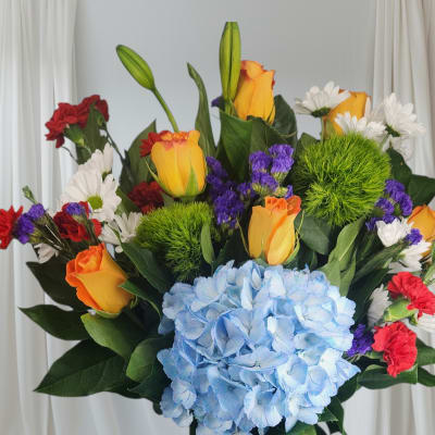 Colorful bouquet with blue hydrangea, roses, carnations, and daisies in a blue vase