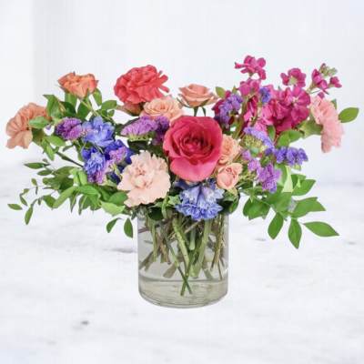 Mixed bouquet of roses, carnations, and purple flowers in a glass vase