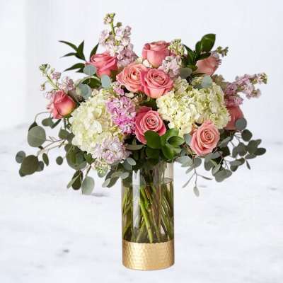 Pink roses and white hydrangeas in a tall glass vase with a gold base