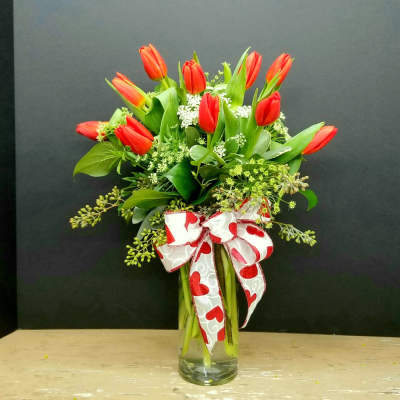 Red tulips in a clear glass vase with a heart-patterned ribbon