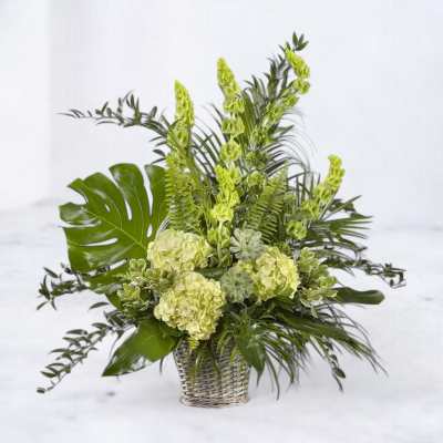 Green floral arrangement in a woven basket with hydrangeas and tropical leaves