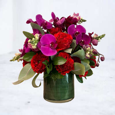 Red roses and purple orchids arranged in a green glass vase