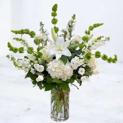 White lilies and hydrangeas in a clear glass vase with green snapdragons