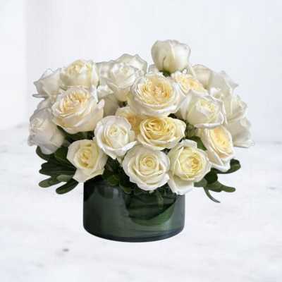 Low arrangement of white and cream roses in a dark green glass cylinder vase