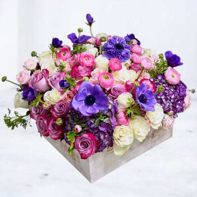 Mixed pink, white, and purple flowers arranged in a square wooden box