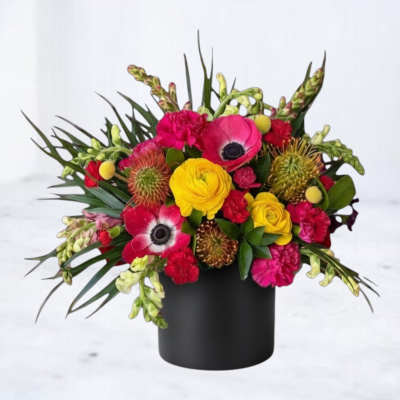Bright mixed bouquet in a black cylindrical vase with yellow, pink, and red blooms