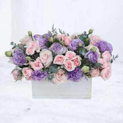 Low arrangement of pink roses and lavender lisianthus in a white rectangular wooden box
