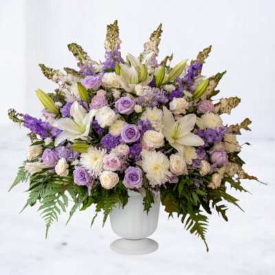 Large lavender and white flower arrangement in a white pedestal urn