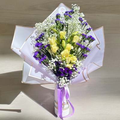 Bouquet of yellow flowers and purple filler wrapped in white paper