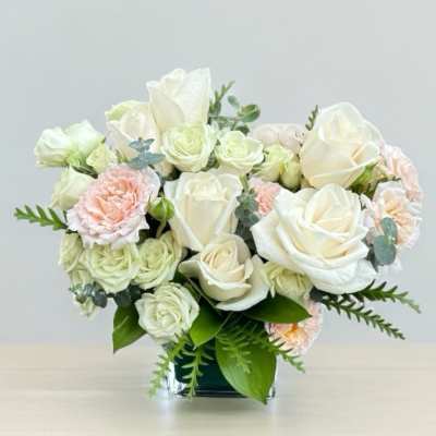 White roses and pale pink carnations in a clear square vase
