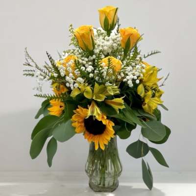 Yellow roses and sunflowers in a clear glass vase
