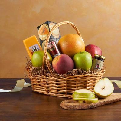 Wicker gift basket with assorted fruit, cheese, sausage, crackers, and jam beside a sliced pear.