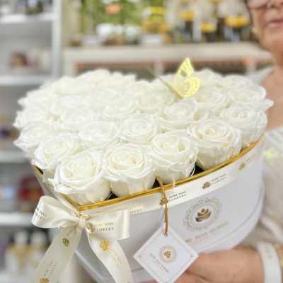 Heart-shaped white box filled with white roses, tied with a white ribbon and tag.