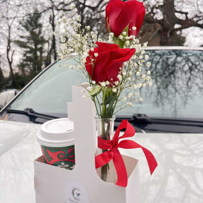 Two red roses in a small glass vase with baby's breath and a red ribbon