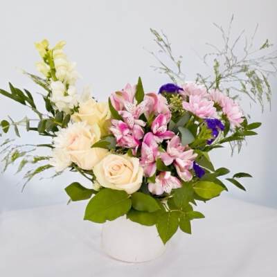 Mixed bouquet of roses, lilies, and pink flowers in a white vase
