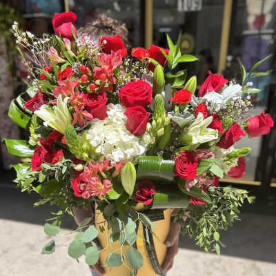 Large arrangement of red roses, lilies, and white hydrangeas in a yellow hatbox-style container