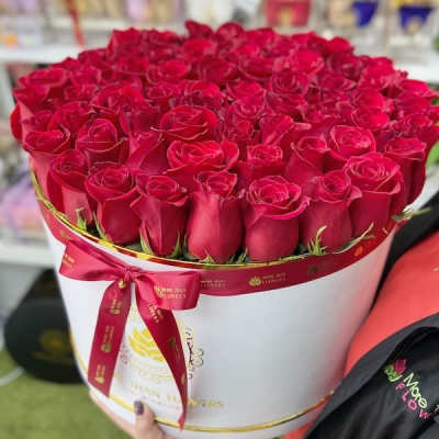 Large round box filled with tightly packed red roses, wrapped with a red ribbon