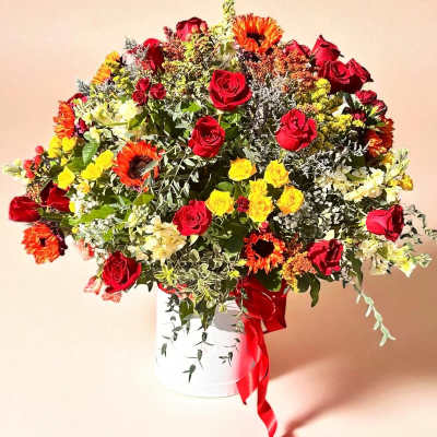 Large bouquet of red and yellow flowers in a white container with a red ribbon