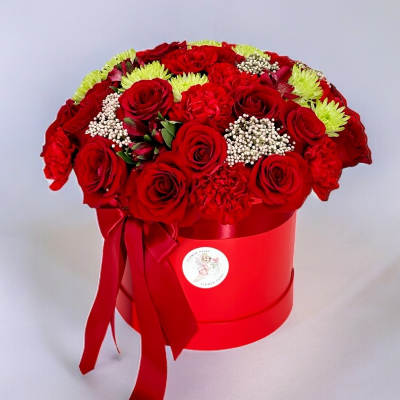 Red roses and carnations arranged in a red hat box with a ribbon