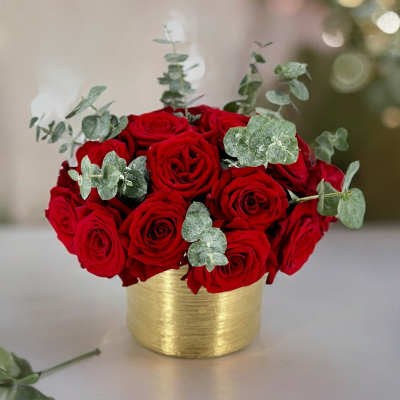 Red roses in a gold container with eucalyptus accents