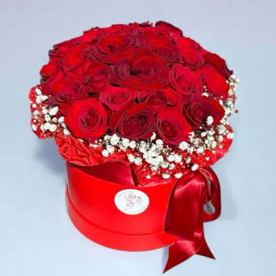 Red roses arranged in a round red hat box with a satin ribbon